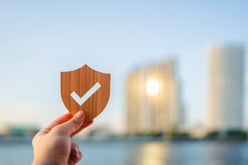 Person holding a small wooden shield up with blurry city building in the background